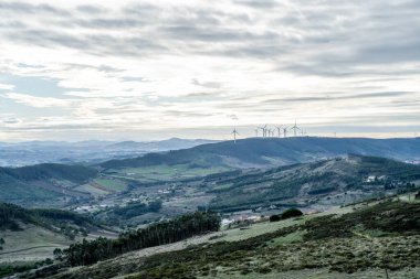 Dar bir toprak yol çimenli bir tepeye tırmanır küçük bir tepe yapısına doğru. Elektrik hatları sırtı geçiyor..