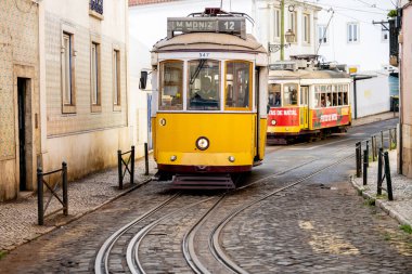 Lizbon Portekiz Aralık 05, 2025. Sarı bir elektrikli tramvay Alfama 'da dar bir kaldırım taşı caddesi boyunca yaklaşıyor..
