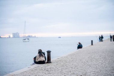 Lizbon Portekiz, Aralık 06: 25. İnsanlar bulutlu bir öğleden sonra Tagus nehrinin kenarında nehir kenarında oturup yürüyorlar..