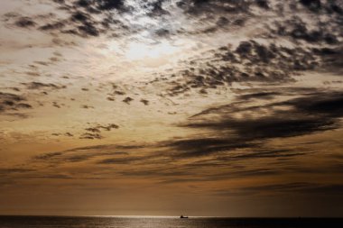 Atlas Okyanusu 'nun üzerinde ufka yakın küçük bir tekneyle gökyüzü boyunca uzanan altın ve kara bulutlar.