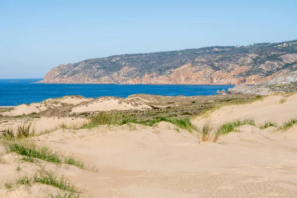Soft sand dunes with sparse grass leading toward the Atlantic Ocean horizon near Guincho Cascais Portugal.