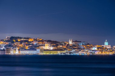Lisbon Portugal December 24 2025. Cargo ship moves along the Tagus River with illuminated Lisbon waterfront visible in the distance.