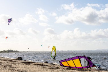 Alcochete Portekiz 19 Aralık 2025. Diğer sürücüler bulutlu gökyüzünün altında Tagus nehrinde yol alırken rüzgar sörfü kumlu sahilde uzanır..