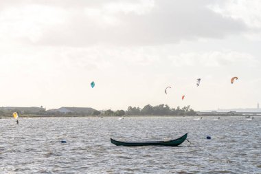 Alcochete Lizbon, 19 Aralık 2025. Uçurtmacılar Tagus nehrinde rüzgarlı su koşullarına biniyorlar ve arka planda kıyı binaları var..