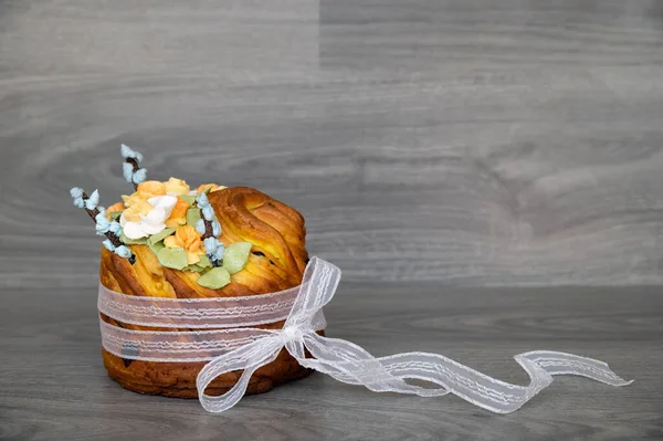 Bread or Easter cake on a gray wooden surface or table. It is decorated with an openwork ribbon and spring marshmallow flowers. Mix of white and yellow daffodils and willow twigs