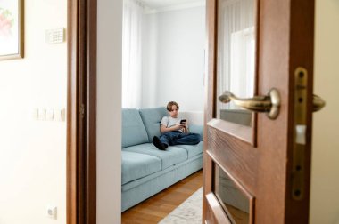 Öğleden sonra rahat oturma odasındaki kanepede dinlenirken akıllı telefon kullanan bir genç.