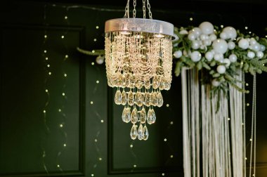 Tavandan sarkan temiz damlaları olan bir avize. Duvarlar karanlıktır, ve çiçekler etrafında ışıklar parıldar. Atmosfer şenlikli ve toplanmaya davet edici..