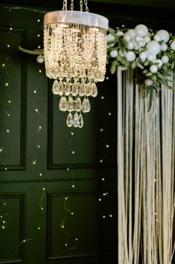 Tavandan sarkan boncuklardan ve kristal damlacıklardan yapılmış bir avize. İp ışıkları arka planda parıldıyor. Çiçek aranjmanı bir olay için ayara detay ekler.