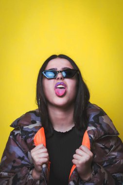 Dilinden sarkan sarı arka planlı güneş gözlüklü bir genç..