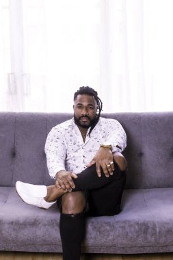 Kanepede oturan siyah tenli adam kameraya bakıyor..