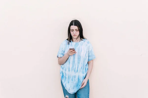 Teen girl in a tie dye shirt on a pinched orange wall looking at the smartphone