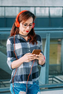 Gözlüklü kadın kulaklıkla müzik dinlerken akıllı telefona bakıyor..