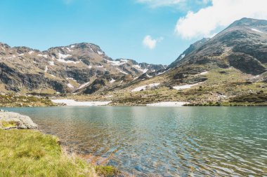 Arka planda mavi gökyüzü olan dağlar arasındaki göl manzarası.