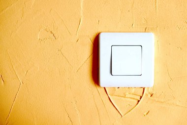 Sarı bir duvarda beyaz ışık düğmesi.