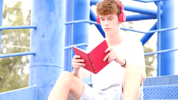 Adolescent Lisant Livre Rouge Avec Des Écouteurs Rouges — Video
