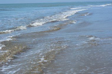 Yuvarlanan dalgalar ve yumuşak kum üzerinde beyaz deniz köpüğü olan tropikal kıyı şeridi yaz seyahatleri, tatiller ve kıyı arkaplanları için mükemmel..
