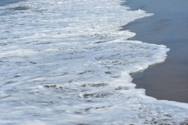 Yuvarlanan dalgalar ve yumuşak kum üzerinde beyaz deniz köpüğü olan tropikal kıyı şeridi yaz seyahatleri, tatiller ve kıyı arkaplanları için mükemmel..