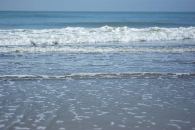 Beyaz köpüklü yumuşak okyanus dalgaları pürüzsüz kumlu sahil yüzeyinde akıyor, yaz ve seyahat temaları için temiz bir doğal kıyı dokusu yaratıyor..
