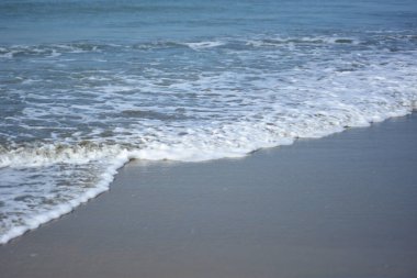 Beyaz köpüklü yumuşak okyanus dalgaları pürüzsüz kumlu sahil yüzeyinde akıyor, yaz ve seyahat temaları için temiz bir doğal kıyı dokusu yaratıyor..