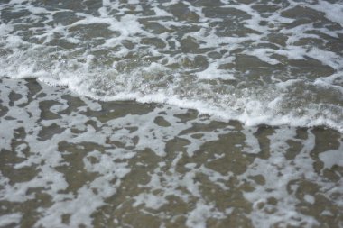 Beyaz köpüklü yumuşak okyanus dalgaları pürüzsüz kumlu sahil yüzeyinde akıyor, yaz ve seyahat temaları için temiz bir doğal kıyı dokusu yaratıyor..