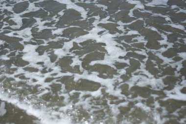 Beyaz köpüklü yumuşak okyanus dalgaları pürüzsüz kumlu sahil yüzeyinde akıyor, yaz ve seyahat temaları için temiz bir doğal kıyı dokusu yaratıyor..