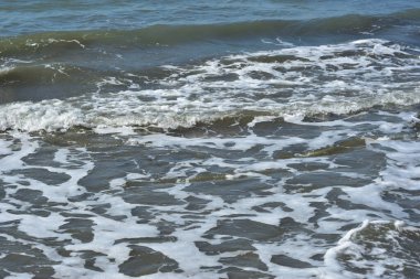 Beyaz köpüklü yumuşak okyanus dalgaları pürüzsüz kumlu sahil yüzeyinde akıyor, yaz ve seyahat temaları için temiz bir doğal kıyı dokusu yaratıyor..