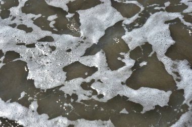 Beyaz köpüklü yumuşak okyanus dalgaları pürüzsüz kumlu sahil yüzeyinde akıyor, yaz ve seyahat temaları için temiz bir doğal kıyı dokusu yaratıyor..