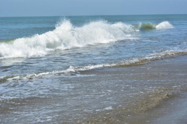 Beyaz köpüklü yumuşak okyanus dalgaları pürüzsüz kumlu sahil yüzeyinde akıyor, yaz ve seyahat temaları için temiz bir doğal kıyı dokusu yaratıyor..