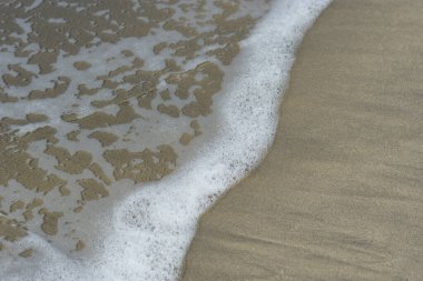 Beyaz köpüklü yumuşak okyanus dalgaları pürüzsüz kumlu sahil yüzeyinde akıyor, yaz ve seyahat temaları için temiz bir doğal kıyı dokusu yaratıyor..
