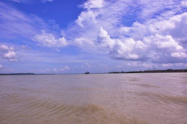 Cox 's Bazar, Bangladeş' teki Bakkhali Nehri 'nin nefes kesici manzarası. Büyük beyaz kümülüs bulutları, uzak yeşil bir mangrov orman hattı üzerinde derin mavi bir gökyüzüne yükselir ve sakin suları yansıtır..