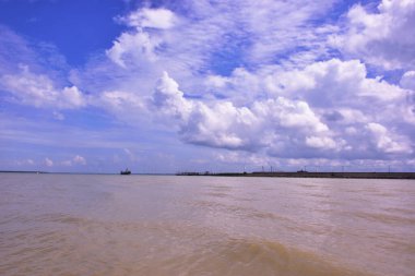 Tüylü beyaz bulutların çamurlu tropikal bir nehrin üzerinde yansıdığı parlak mavi bir gökyüzünün güzel dikey arka planı. Seyahat veya hava durumu tasarımları için mükemmel kopyalama alanı.