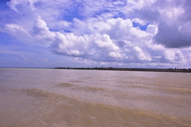 Cox 's Bazar, Bangladeş' teki Bakkhali Nehri 'nin nefes kesici manzarası. Büyük beyaz kümülüs bulutları, uzak yeşil bir mangrov orman hattı üzerinde derin mavi bir gökyüzüne yükselir ve sakin suları yansıtır..