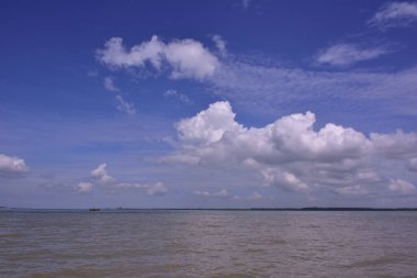 Tüylü beyaz bulutların çamurlu tropikal bir nehrin üzerinde yansıdığı parlak mavi bir gökyüzünün güzel dikey arka planı. Seyahat veya hava durumu tasarımları için mükemmel kopyalama alanı.