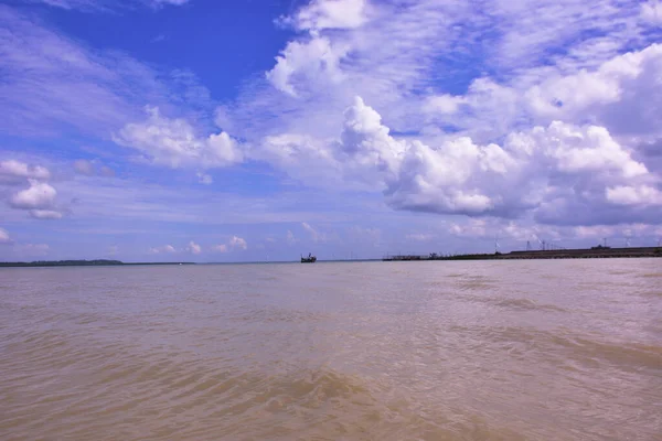 Cox 's Bazar, Bangladeş' teki Bakkhali Nehri 'nin nefes kesici manzarası. Büyük beyaz kümülüs bulutları, uzak yeşil bir mangrov orman hattı üzerinde derin mavi bir gökyüzüne yükselir ve sakin suları yansıtır..