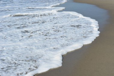 Cox 's Bazar, Bangladeş' teki Laboni Sahili 'nin altın kumlarını kaplayan yumuşak beyaz bir dalganın çıtır çıtır bir yakın çekimi, dünyanın en uzun doğal deniz sahili, parlak sahil gün ışığı altında..