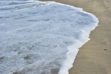 Cox 's Bazar, Bangladeş' teki Laboni Sahili 'nin altın kumlarını kaplayan yumuşak beyaz bir dalganın çıtır çıtır bir yakın çekimi, dünyanın en uzun doğal deniz sahili, parlak sahil gün ışığı altında..