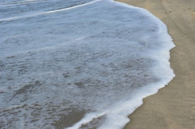 Cox 's Bazar, Bangladeş' teki Laboni Sahili 'nin altın kumlarını kaplayan yumuşak beyaz bir dalganın çıtır çıtır bir yakın çekimi, dünyanın en uzun doğal deniz sahili, parlak sahil gün ışığı altında..