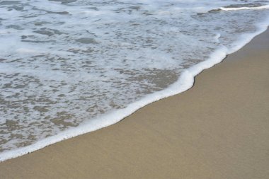 Cox 's Bazar, Bangladeş' teki Laboni Sahili 'nin altın kumlarını kaplayan yumuşak beyaz bir dalganın çıtır çıtır bir yakın çekimi, dünyanın en uzun doğal deniz sahili, parlak sahil gün ışığı altında..