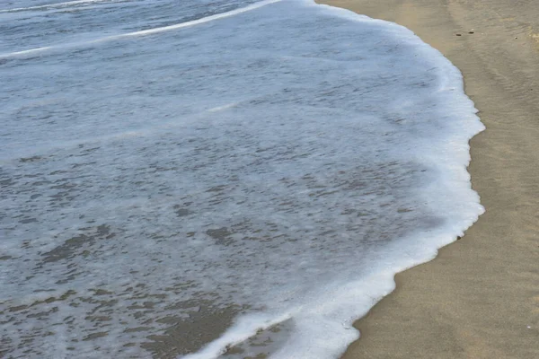 Cox 's Bazar, Bangladeş' teki Laboni Sahili 'nin altın kumlarını kaplayan yumuşak beyaz bir dalganın çıtır çıtır bir yakın çekimi, dünyanın en uzun doğal deniz sahili, parlak sahil gün ışığı altında..