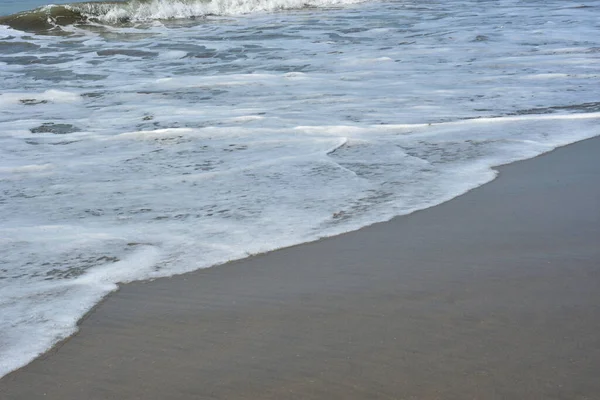 Cox 's Bazar, Bangladeş' teki Laboni Sahili 'nin altın kumlarını kaplayan yumuşak beyaz bir dalganın çıtır çıtır bir yakın çekimi, dünyanın en uzun doğal deniz sahili, parlak sahil gün ışığı altında..