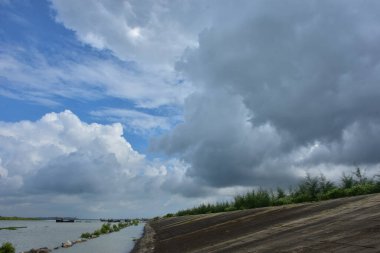 Mavi gökyüzüne karşı parlak beyaz kümülüs bulutlarının yer aldığı güzel bir sahil su yolu. Bangladeş kırsalında temiz su ve yemyeşil alan mükemmel bir yaz gününü yakalıyor..