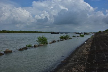 Mavi gökyüzüne karşı parlak beyaz kümülüs bulutlarının yer aldığı güzel bir sahil su yolu. Bangladeş kırsalında temiz su ve yemyeşil alan mükemmel bir yaz gününü yakalıyor..
