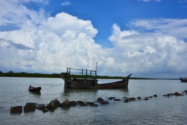 Mavi gökyüzüne karşı parlak beyaz kümülüs bulutlarının yer aldığı güzel bir sahil su yolu. Bangladeş kırsalında temiz su ve yemyeşil alan mükemmel bir yaz gününü yakalıyor..