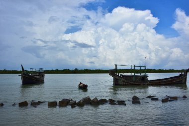 Mavi gökyüzüne karşı parlak beyaz kümülüs bulutlarının yer aldığı güzel bir sahil su yolu. Bangladeş kırsalında temiz su ve yemyeşil alan mükemmel bir yaz gününü yakalıyor..