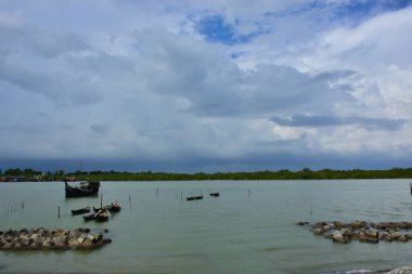 Mavi gökyüzüne karşı parlak beyaz kümülüs bulutlarının yer aldığı güzel bir sahil su yolu. Bangladeş kırsalında temiz su ve yemyeşil alan mükemmel bir yaz gününü yakalıyor..