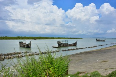Mavi gökyüzüne karşı parlak beyaz kümülüs bulutlarının yer aldığı güzel bir sahil su yolu. Bangladeş kırsalında temiz su ve yemyeşil alan mükemmel bir yaz gününü yakalıyor..