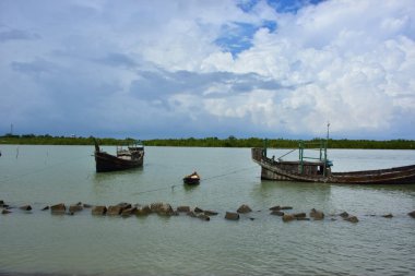 Bangladeş 'teki engin bir nehrin geniş açılı görüntüsü dramatik, bulutlu bir gökyüzü altında. Karanlık bulutlar muson mevsiminde sakin su üzerinde güçlü bir atmosfer yaratırlar..