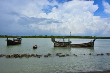 Bangladeş 'teki engin bir nehrin geniş açılı görüntüsü dramatik, bulutlu bir gökyüzü altında. Karanlık bulutlar muson mevsiminde sakin su üzerinde güçlü bir atmosfer yaratırlar..
