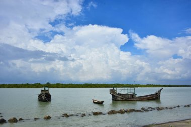 Bangladeş 'teki engin bir nehrin geniş açılı görüntüsü dramatik, bulutlu bir gökyüzü altında. Karanlık bulutlar muson mevsiminde sakin su üzerinde güçlü bir atmosfer yaratırlar..