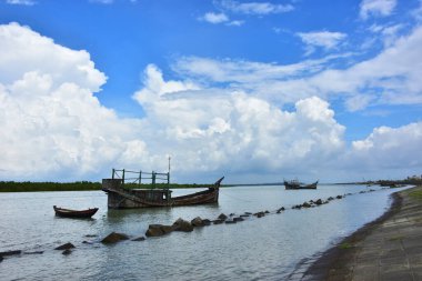 Bangladeş 'teki engin bir nehrin geniş açılı görüntüsü dramatik, bulutlu bir gökyüzü altında. Karanlık bulutlar muson mevsiminde sakin su üzerinde güçlü bir atmosfer yaratırlar..